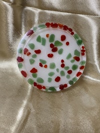 a red, green and white glass coaster on a satin sheet