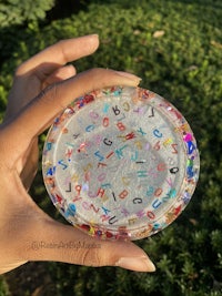 a person holding up a glass plate with colorful letters on it